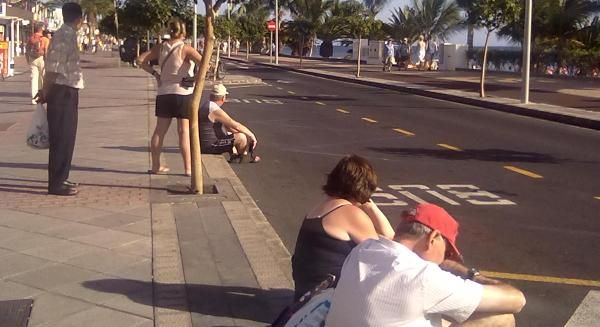 La falta de una parada de guaguas en Puerto del Carmen obliga a los turistas a esperar sentados en la acera a pleno sol