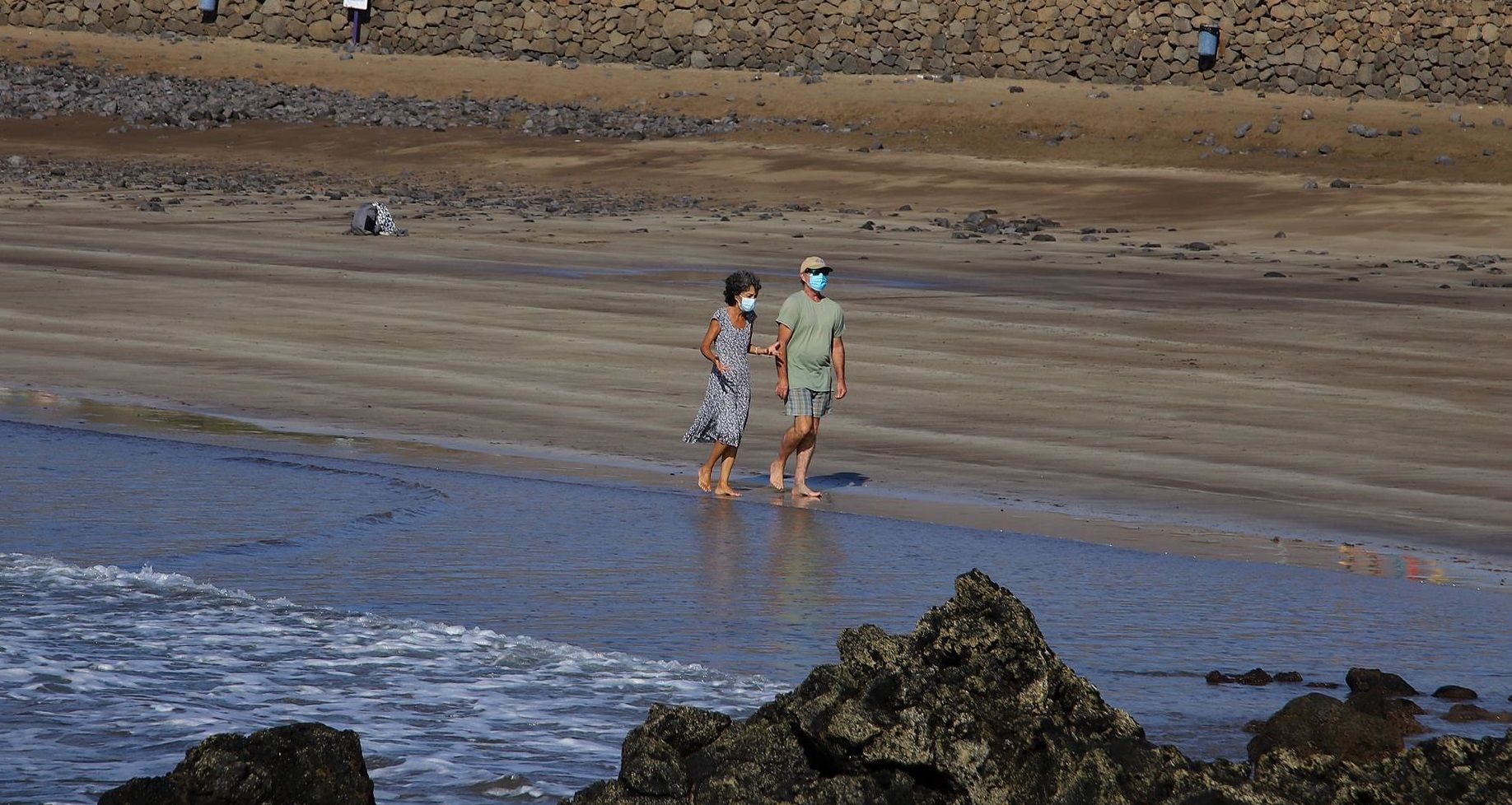 Una pareja pasea con mascarilla por la playa de Arrieta por la crisis del coronavirus