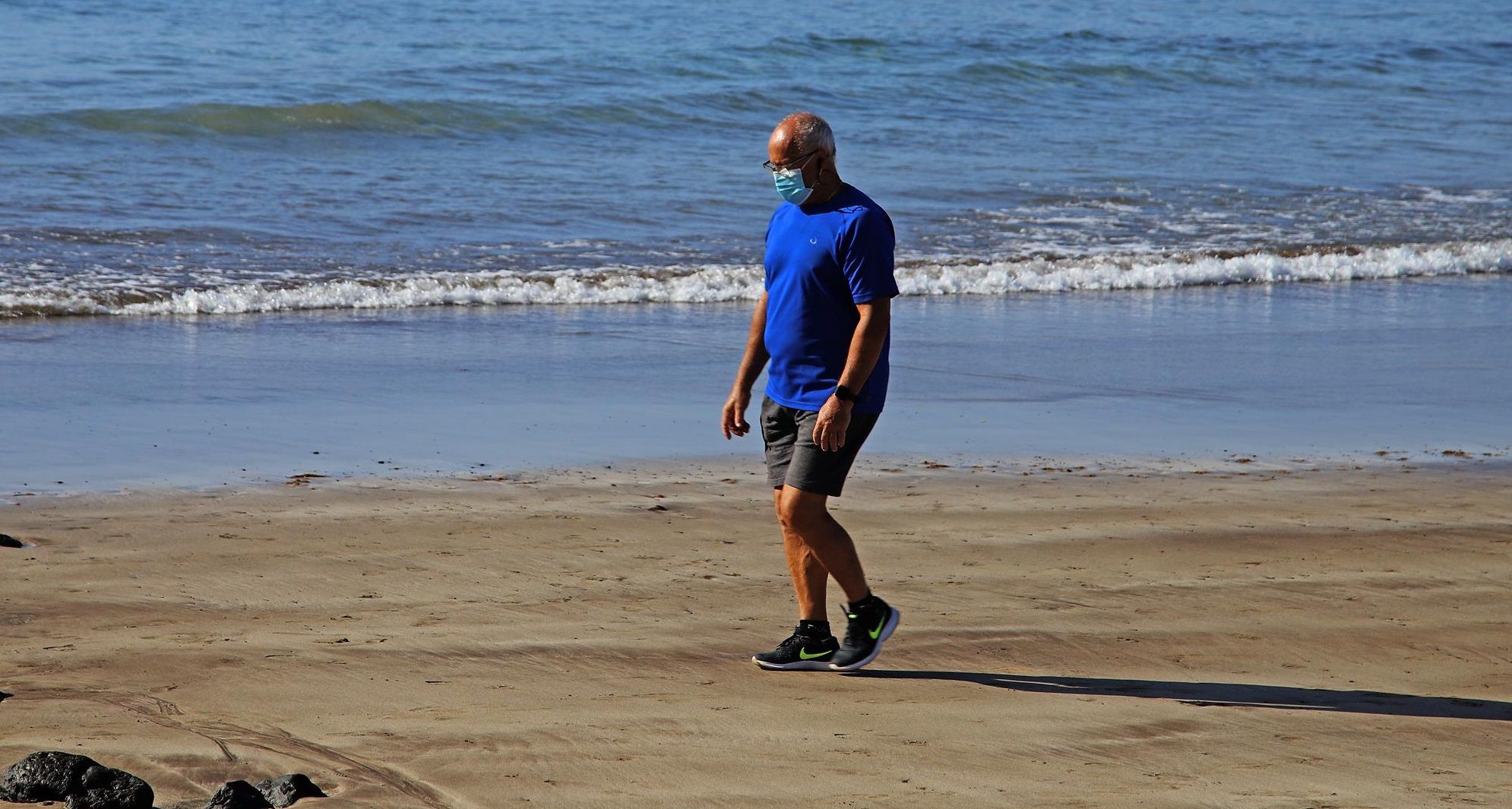 Un hombre pasea con mascarilla por la playa durante la crisis del coronavirus en Lanzarote