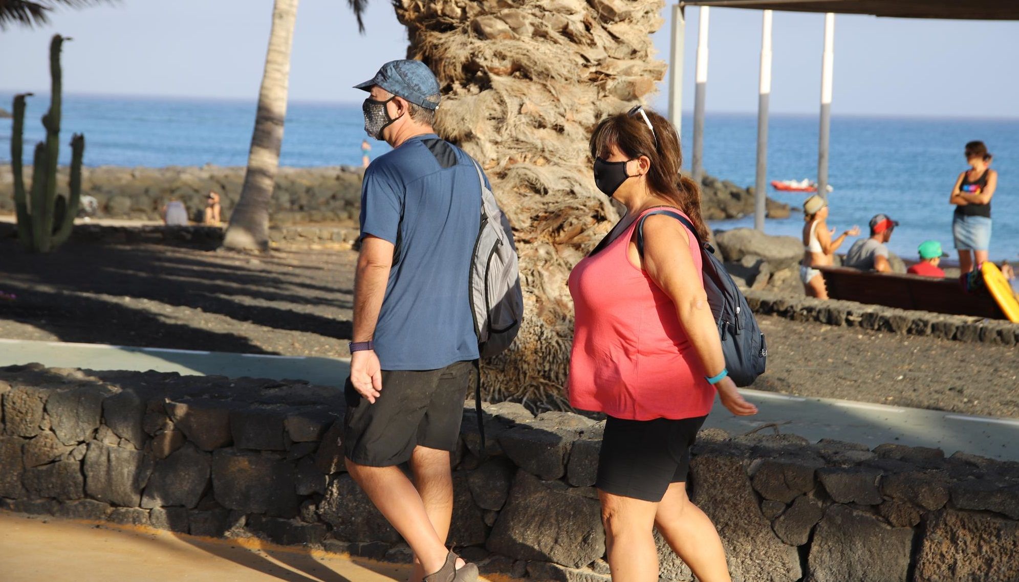 Una pareja con mascarilla pasea junto a la playa de Costa Teguise durante la crisis del coronavirus