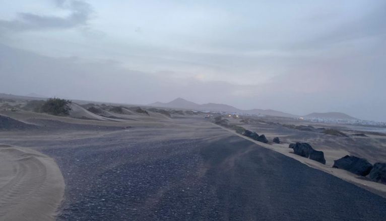 Imagen de la carretera de Famara cubiera de arena durante un temporal de viento