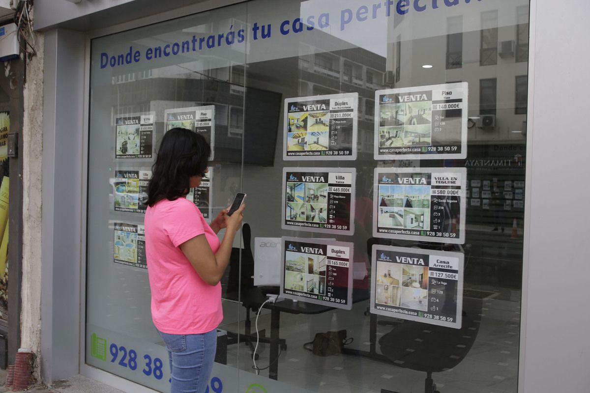 Una mujer consulta ofertas de viviendas en venta en el escaparate de una inmobiliaria de Lanzarote