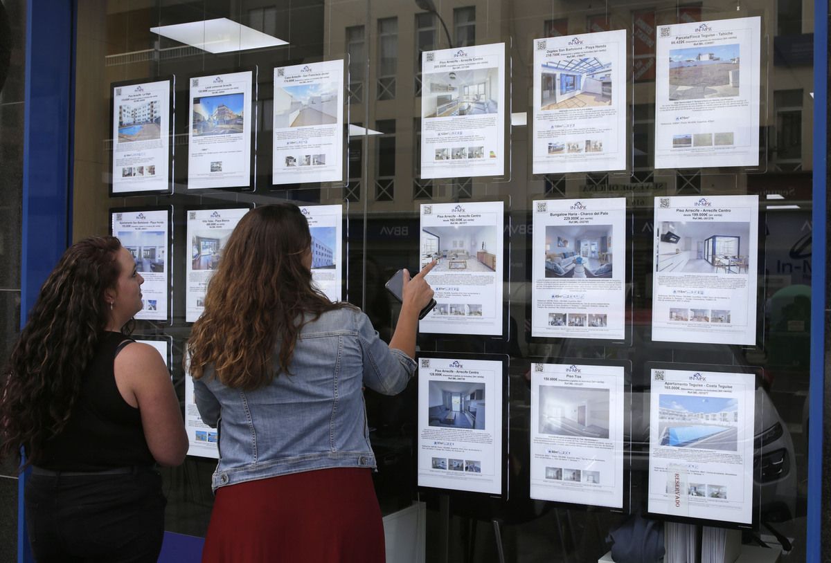 Dos jóvenes comparan opciones de vivienda en una agencia inmobiliaria Dos jóvenes comparan opciones de vivienda en una agencia inmobiliaria