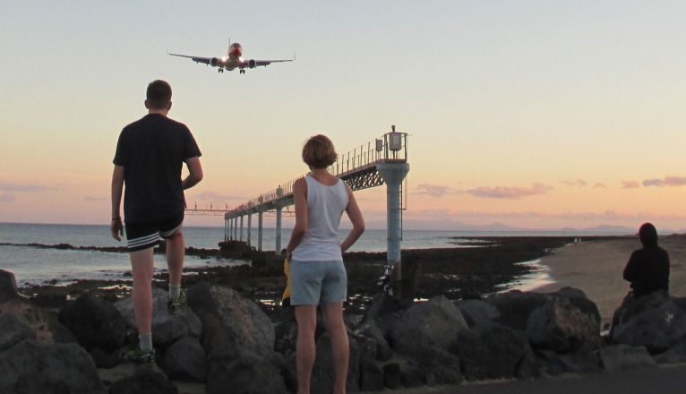 Turistas viendo aterrizar los aviones desde la playa
