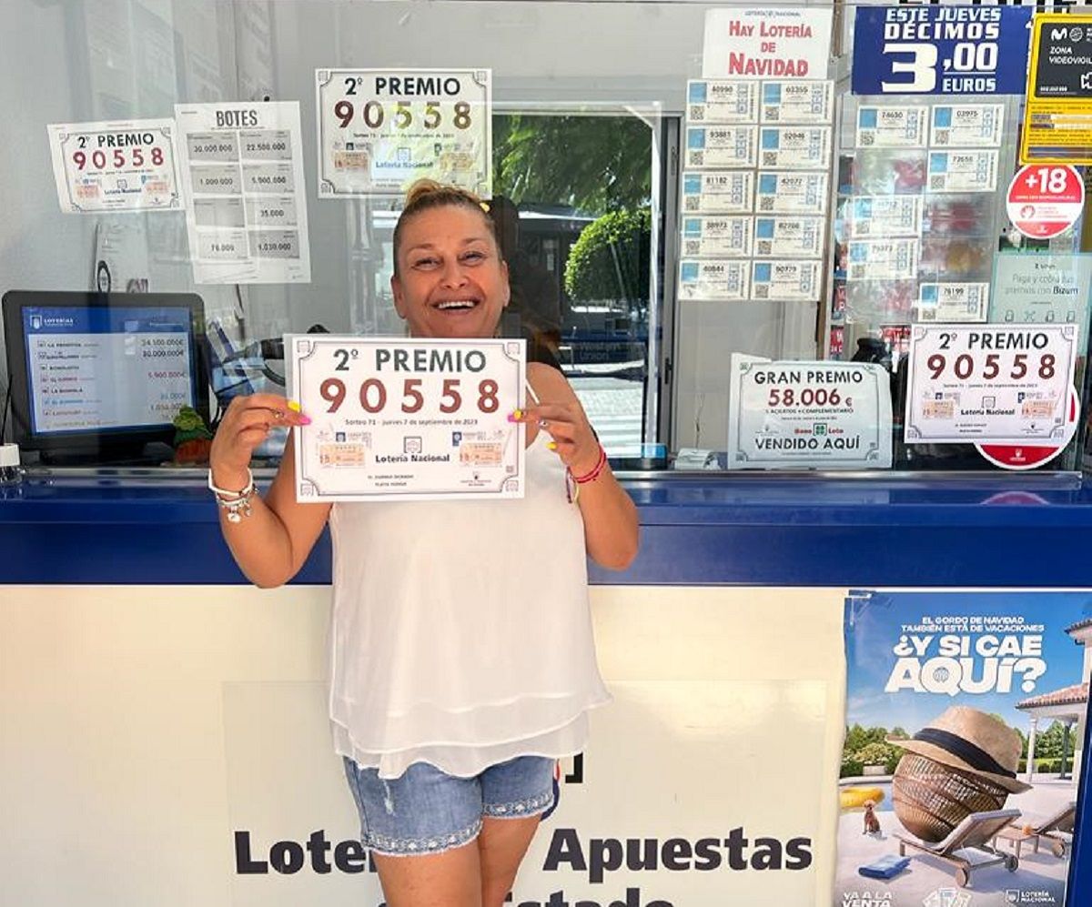 La dependienta Tina de Ganzo Noda posa junto al número agraciado en la administración de lotería El Duende Dorado