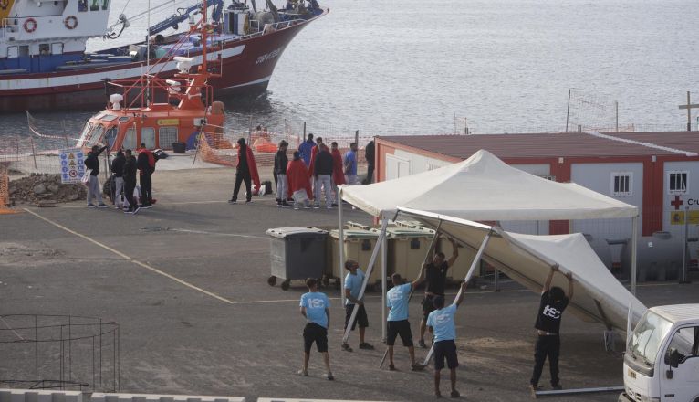 Varias personas trabajan en el montaje de carpas con un grupo de personas migrantes al fondo en Puerto Naos. Foto: José Luis Carrasco.