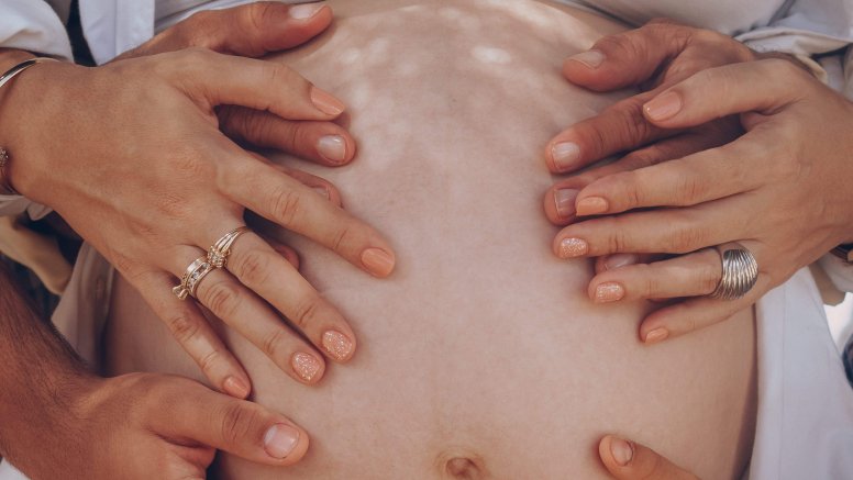 Una familia pone las manos en el vientre de una mujer embarazada. Foto: Elias Suárez (Pexels).