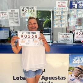 La dependienta Tina de Ganzo Noda posa junto al número agraciado en la administración de lotería El Duende Dorado