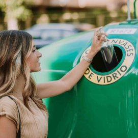 Una mujer deposita una botella de vidrio en un contenedor.