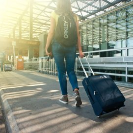 Una mujer se dirige a un aeropuerto con mochila y trolley